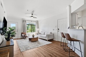 Un salon moderne comprenant un canapé, une table basse et des fauteuils, un téléviseur et une grande fenêtre avec des rideaux.