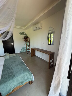 Ein Schlafzimmer mit einem Bett, einer Bank, einem Spiegel und einer Zimmerpflanze.