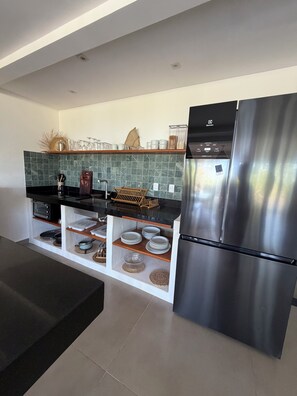 Eine moderne Küche mit einem Edelstahlkühlschrank, einer Mikrowelle und einem eingebauten Backofen. Holzhaltige Regale beherbergen Geschirr, und ein Hängegestell dient zur Aufbewahrung von Küchenutensilien.
