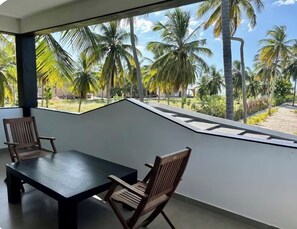 A balcony with a view of palm trees and a sandy beach.