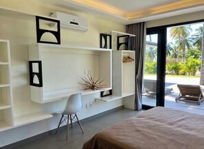 A modern hotel room with a bed, a desk with a chair, built-in shelves, and a view of a palm tree garden.