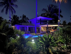 A modern house with a pool surrounded by palm trees at night.