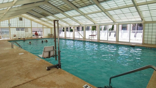 An indoor swimming pool with a glass ceiling, clear water, and a lifeguard stand. - Ocean Lakes Beach House | Ocean View | Free Golf Cart | Sleeps 6 (Myrtle Beach)
