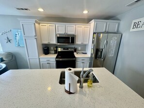 A kitchen with white cabinets, a stainless steel refrigerator, and a microwave. - Ocean Lakes Beach House | Ocean View | Free Golf Cart | Sleeps 6 (Myrtle Beach)