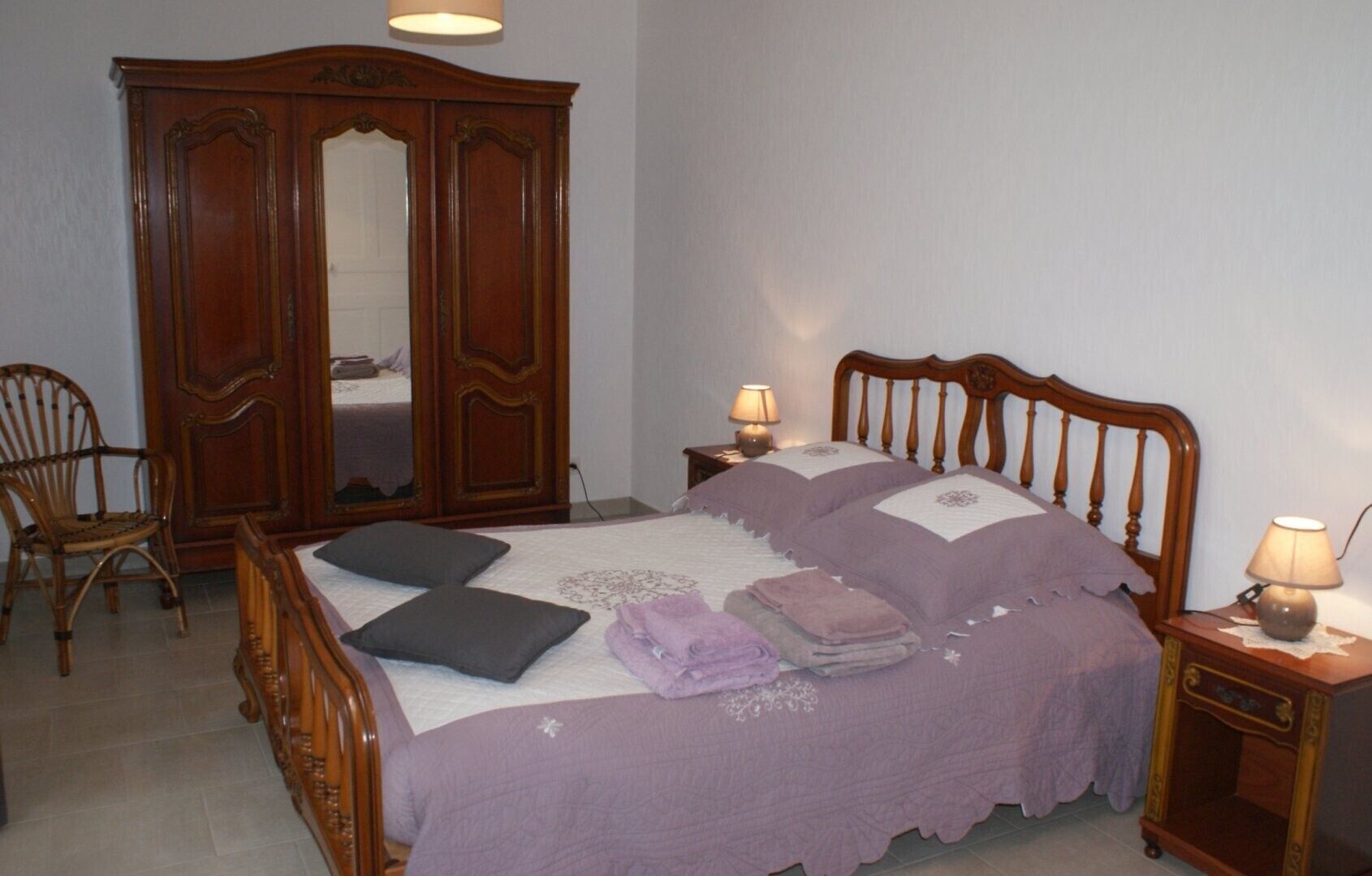 Ein Schlafzimmer mit einem Bett, zwei Nachttischen, einem Holzschrank, einem Sessel und einem Spiegel.