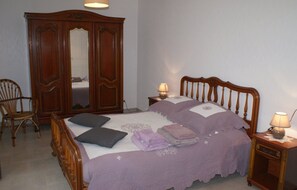 A bedroom with a bed, two nightstands, a wooden wardrobe, a chair, and a mirror.