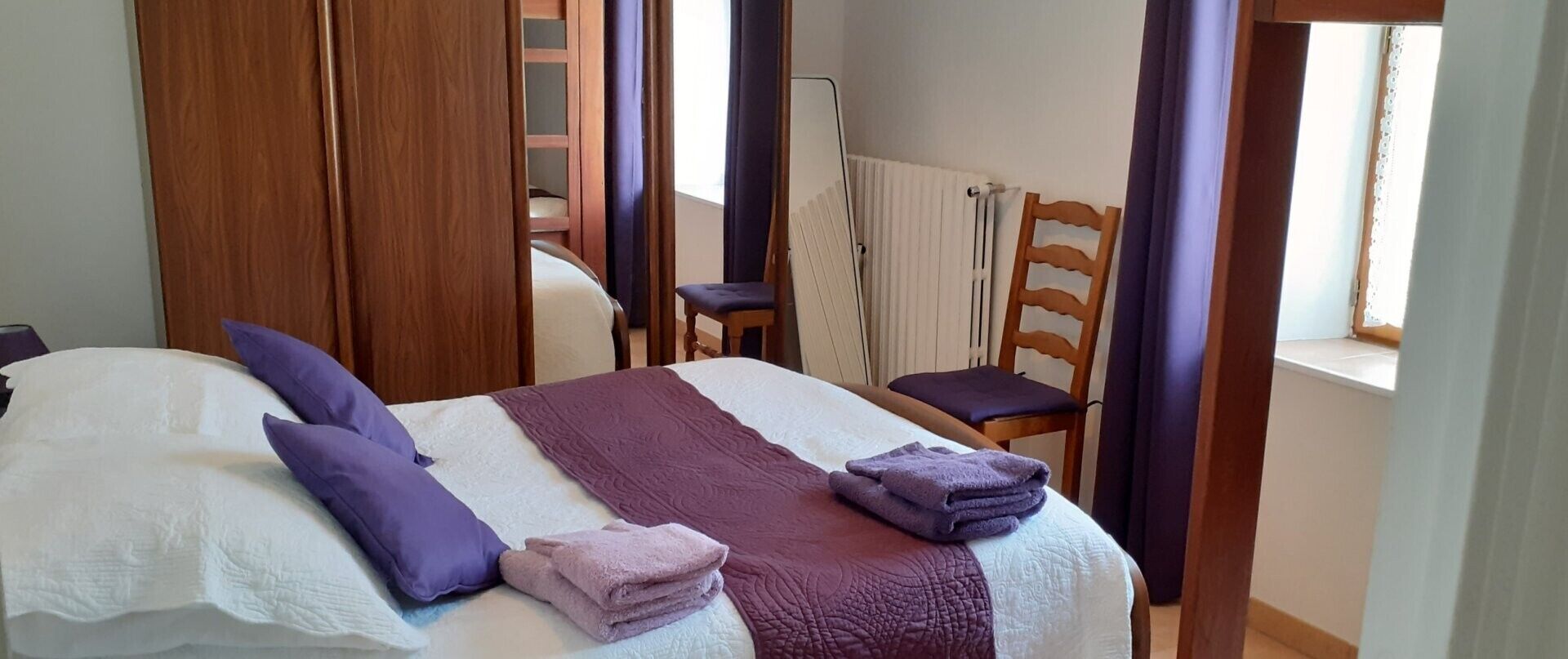 A hotel room with a bed, a chair, a window, and a radiator.