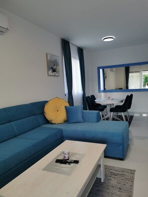 Ein modernes Wohnzimmer mit einem blauen Sofa, einem Couchtisch und einem Essbereich mit kleinem Tisch und Stühlen.