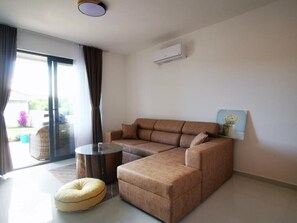 Ein modernes Wohnzimmer mit einem Ecksofa, einem runden Couchtisch und einem großen Fenster mit Vorhängen.