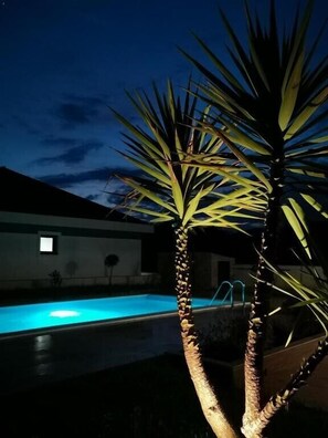 Ein Poolbereich mit einer Palme im Vordergrund und einem Gebäude im Hintergrund.