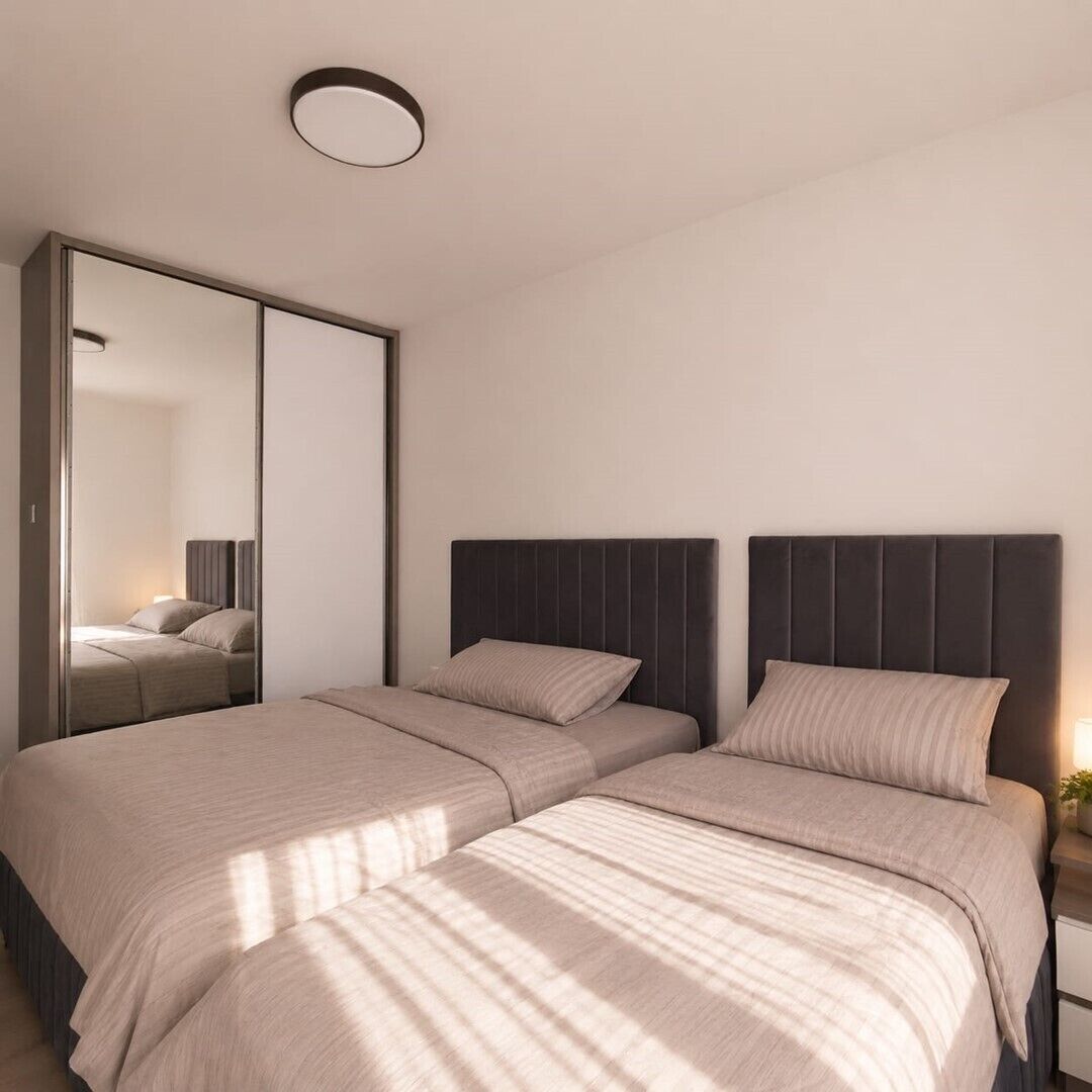 A bedroom with two beds, a large mirror, and a bedside table with a lamp.