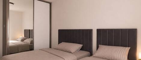 A bedroom with two beds, a large mirror, and a bedside table with a lamp.
