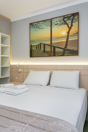 A hotel room with a bed, a nightstand, a wall-mounted shelf, and a painting of a beach scene. - 200m from Beira-Mar | Pool | Dining #CA107 (Florianópolis)