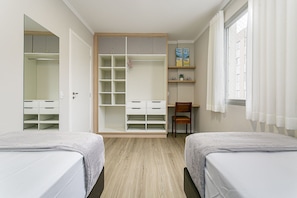 Ein Schlafzimmer mit zwei Betten, einem Kleiderschrank, einem Stuhl und einem Schreibtisch mit Regalen.