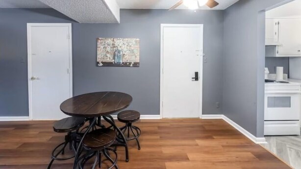 A room with a ceiling fan, a dining table with four chairs, and a kitchen area with cabinets. - Sleek & Peaceful Retreat at Bailey Court #1 (El Dorado)