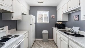 A compact kitchen with white cabinets, a built-in stove, and a window. - Sleek & Peaceful Retreat at Bailey Court #1 (El Dorado)