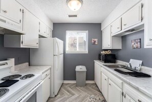 A compact kitchen with white cabinets, a built-in stove, and a window. - Sleek & Peaceful Retreat at Bailey Court #1 (El Dorado)