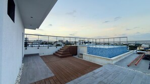 A rooftop terrace with a swimming pool, wooden deck, and city views. - OceanView Luxury Condo Rooftop Pool Near Colonial Zone & Malecon (Santo Domingo)