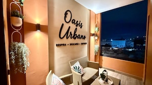 Ein gemütlicher Sitzbereich mit Korbmöbeln und einem an der Wand befestigten Schild mit der Aufschrift 'Oasis Urbano' und Auflistung der Annehmlichkeiten.