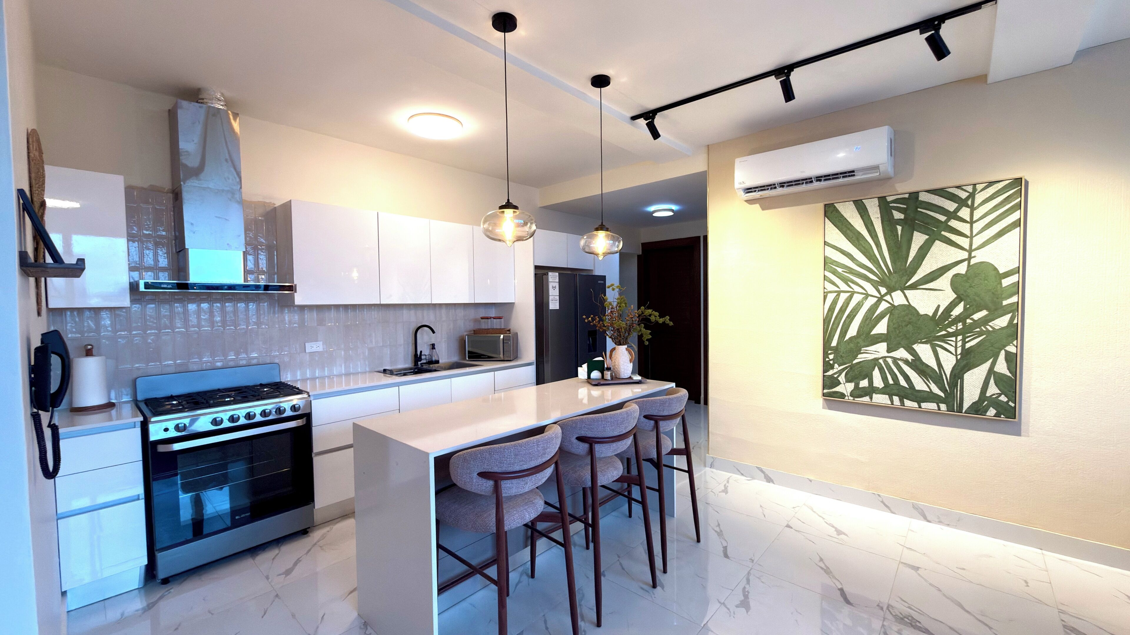 Une cuisine moderne dotée d’un îlot central, d’appareils électroménagers en acier inoxydable, de luminaires suspendus et d’une grande illustration botanique au mur.