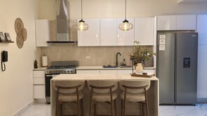 Una cucina moderna con isola centrale, sgabelli da bar, elettrodomestici in acciaio inossidabile e illuminazione a sospensione.