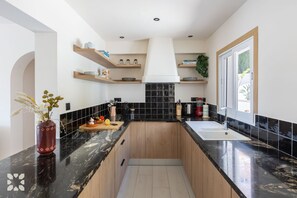 A modern kitchen with black countertops, wooden cabinets, and a central island. - Villa ALMASUR by Abahana Villas (Benissa)