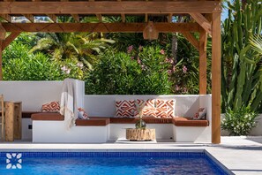 Ein Sitzbereich am Pool mit Pergola, umgeben von üppiger Vegetation und einem klaren, blauen Pool.