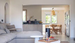 A modern living room with a sofa, a coffee table, and a dining area with chairs and a table. - Villa ALMASUR by Abahana Villas (Benissa)