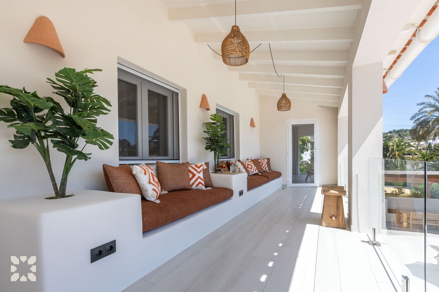 Un intérieur moderne avec un long canapé, de grandes fenêtres et des lampes suspendues en osier.