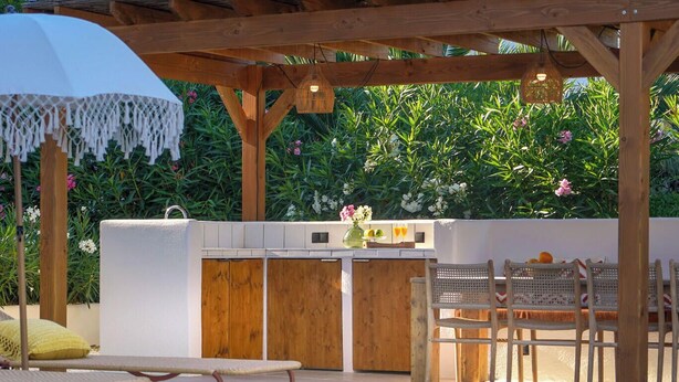 An outdoor kitchen area with a pool, wooden deck, and seating. - Villa ALMASUR by Abahana Villas (Benissa)