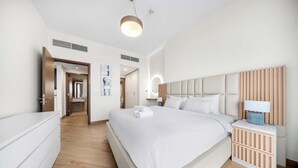 Una habitación de hotel moderna con una cama grande, una mesita de noche con lámpara, un armario y un baño visible a través de una puerta abierta.