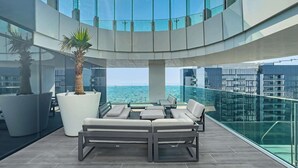 Un área lounge al aire libre moderna con barandilla de vidrio, asientos y vistas de la ciudad.