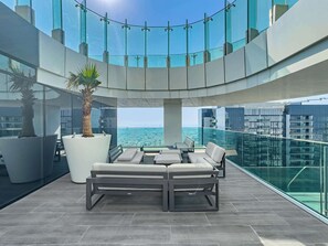 A modern outdoor lounge area with a glass balustrade, seating, and a view of the cityscape. - StayShort - Vibrant 1-Bedroom Apartment at 1 Residences West in Za'abeel (Zabeel)