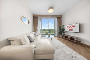 A modern living room with a sectional sofa, a glass coffee table, a flat-screen TV, and a view of the outdoors through large sliding doors. - StayShort - Vibrant 1-Bedroom Apartment at 1 Residences West in Za'abeel (Zabeel)