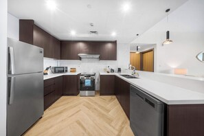 A modern kitchen with stainless steel appliances, wooden cabinets, and a herringbone wood floor. - StayShort - Vibrant 1-Bedroom Apartment at 1 Residences West in Za'abeel (Zabeel)