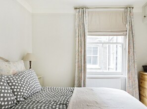 A bedroom with a bed, a nightstand, a dresser, and a window with curtains. - Charming 1BR Chelsea | King Bed | Central Location (london)