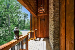 A wooden cabin with a stone wall, a wooden deck, and a bird sculpture.