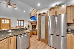 A modern kitchen with a stone fireplace, stainless steel appliances, and wooden cabinetry.