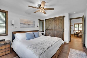 A bedroom with a bed, a ceiling fan, a wooden door, and a painting on the wall.