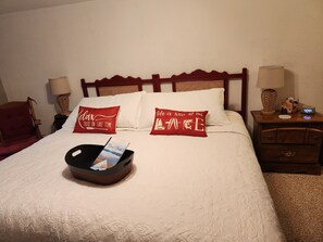 Ein Hotelzimmer mit einem Bett, zwei Kissen, einem Nachttisch mit Lampe und einem Beistelltisch mit einer Uhr.