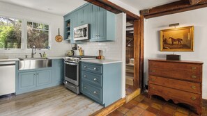 Eine Küche mit blauen Schränken, einem Herd und einer Mikrowelle. Es gibt einen Holzschrank und ein Bild an der Wand.