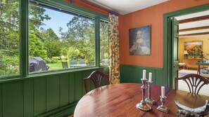 Ein Esszimmer mit Holztisch, Stühlen und Blick auf einen Garten durch große Fenster.