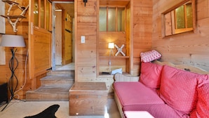 A wooden interior with a sofa, a lamp, a small table, and a staircase.