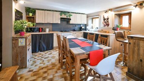 A modern kitchen with wooden cabinets, a central island, and a dining area with a red and black tablecloth.