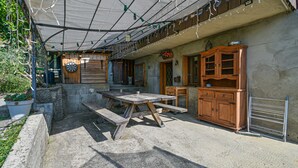 A rustic outdoor patio with a wooden table and benches, a dartboard, and a wooden cabinet.
