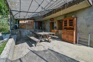 A rustic outdoor patio with a wooden table and benches, a dartboard, and a wooden cabinet.