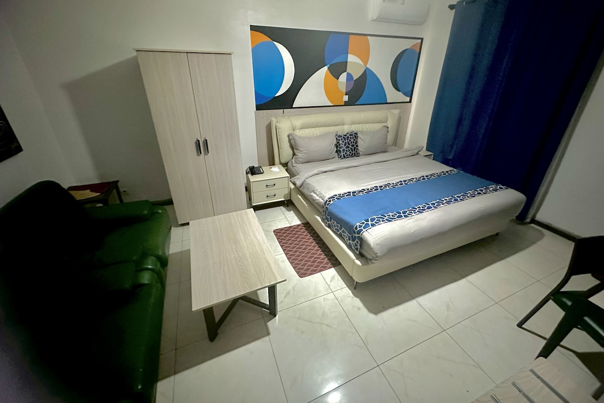 Une chambre d’hôtel avec un lit, une table de chevet, une armoire, une chaise verte et une table.