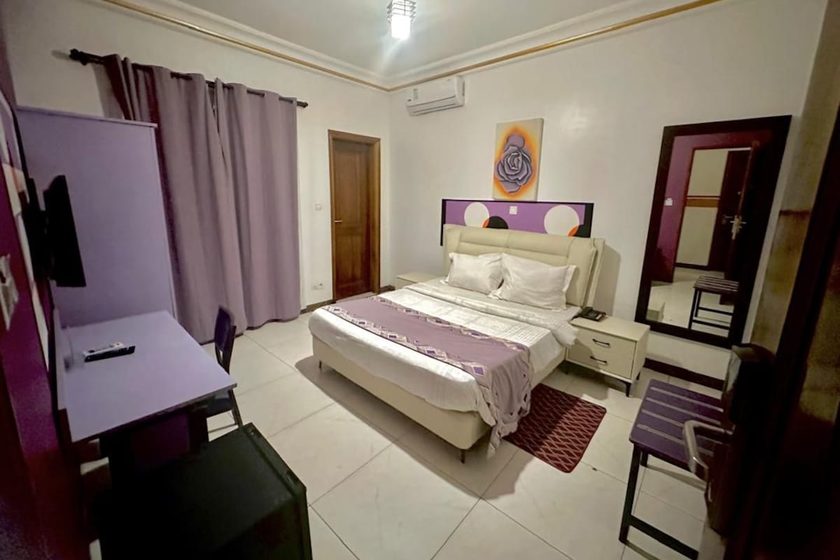 A bedroom with a bed, bedside tables, a desk, a chair, a mirror, and a door.