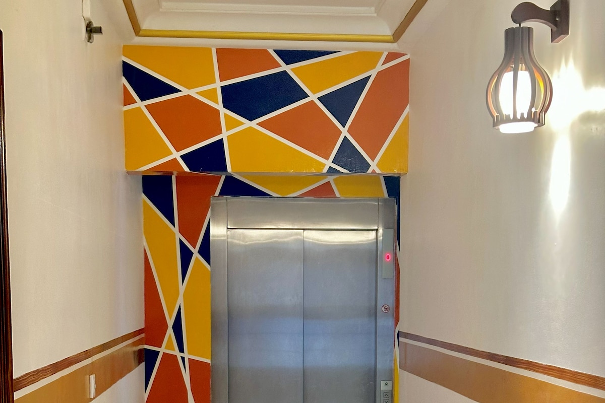 Un couloir doté d’un ascenseur moderne, d’un mur orné de motifs et d’un luminaire.