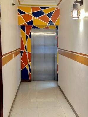 Un couloir doté d’un ascenseur moderne, d’un mur orné de motifs et d’un luminaire.